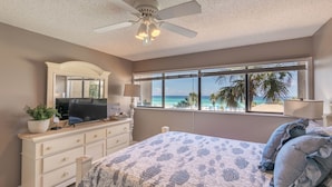 A bedroom with a bed, a dresser, a television, and a window with a beach view.