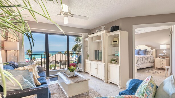 A spacious living room with a large window overlooking a beach, a ceiling fan, and a cozy seating area with a coffee table.