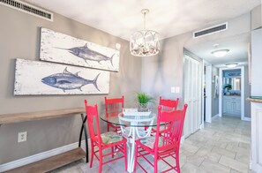 Un comedor con una mesa redonda de vidrio, sillas rojas y dos cuadros de peces colgados en la pared.