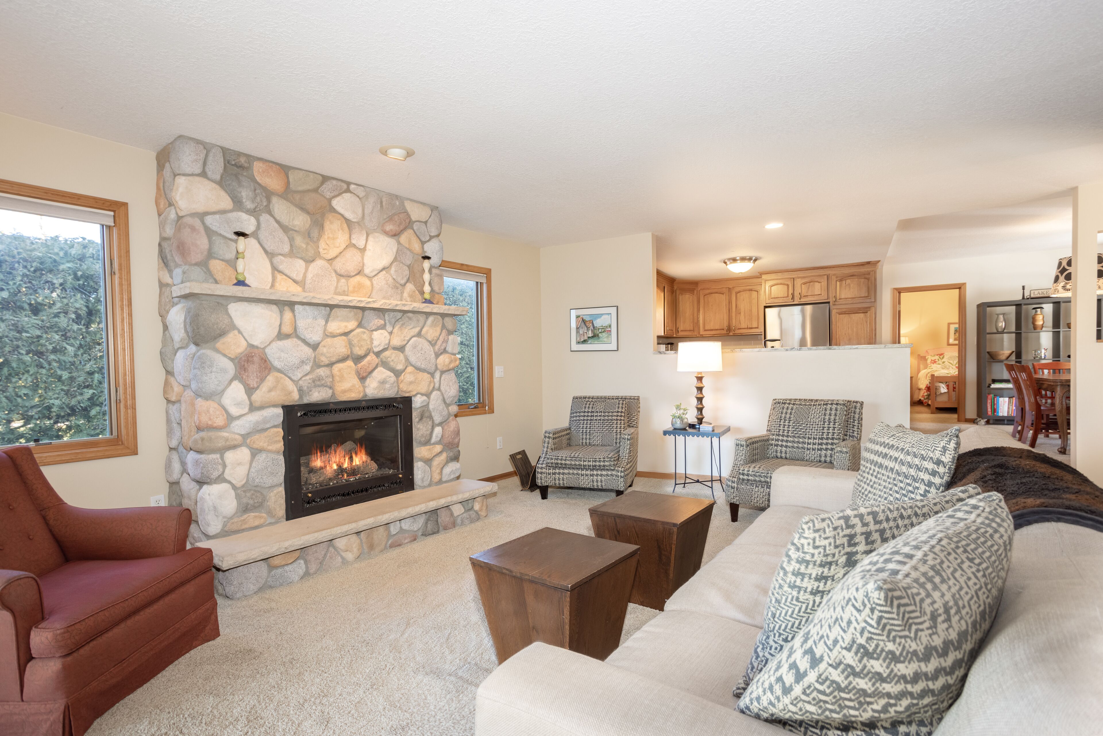 A living room with a stone fireplace, a sofa, a coffee table, and a view of the kitchen.