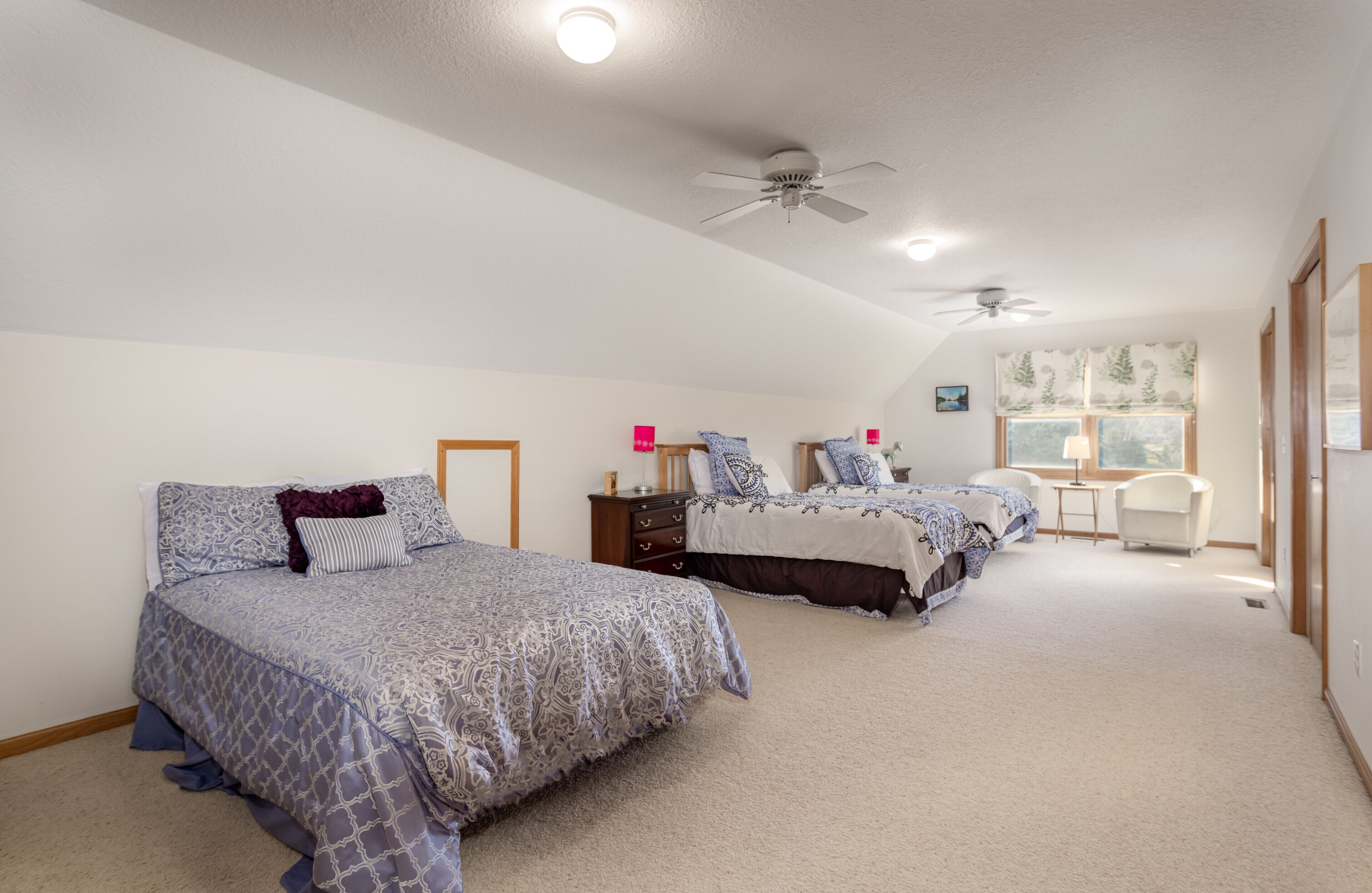 A bedroom with two beds, a ceiling fan, and a window with a view.
