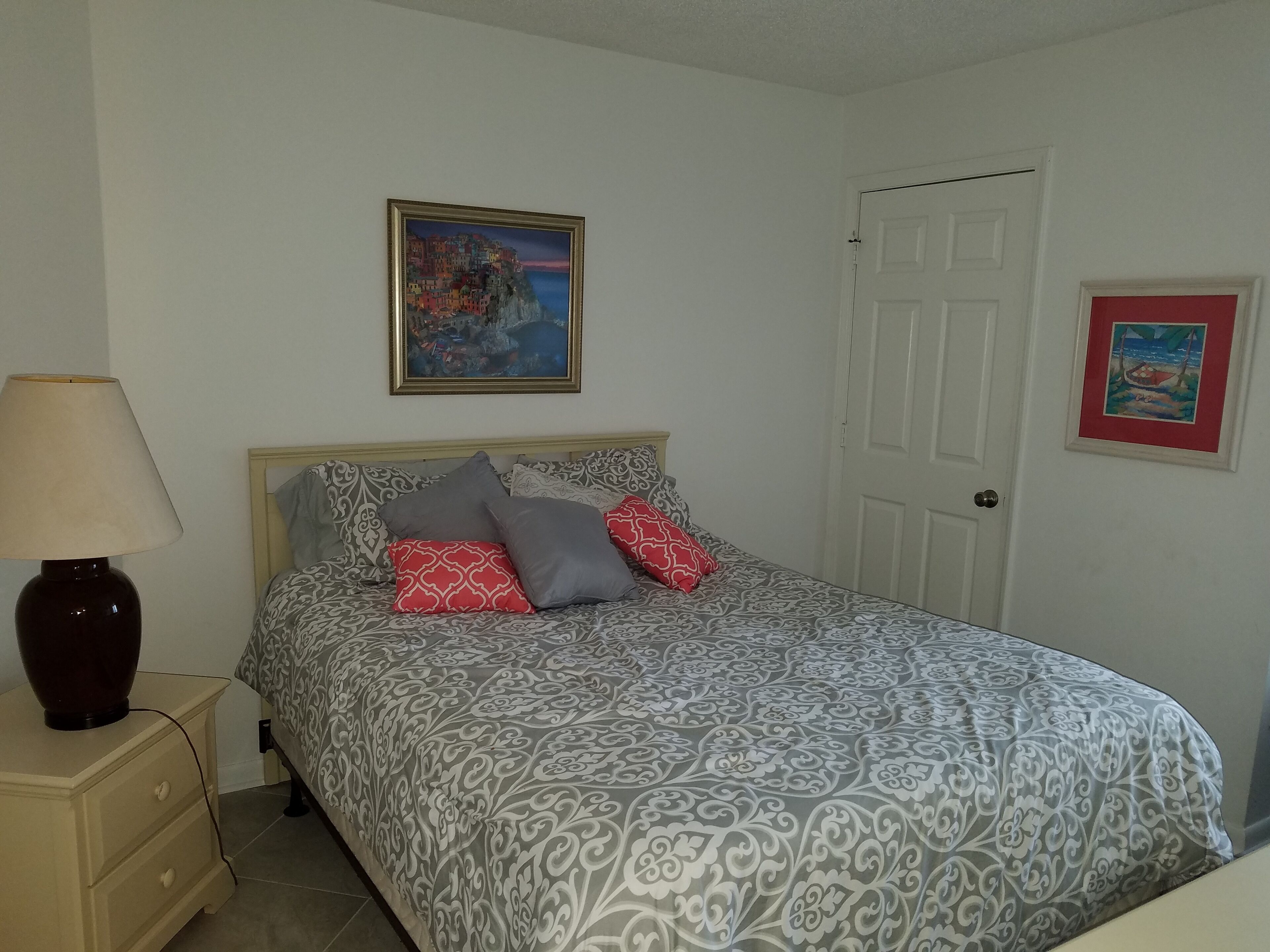 A bedroom with a bed, a nightstand, a lamp, and two framed pictures on the wall.