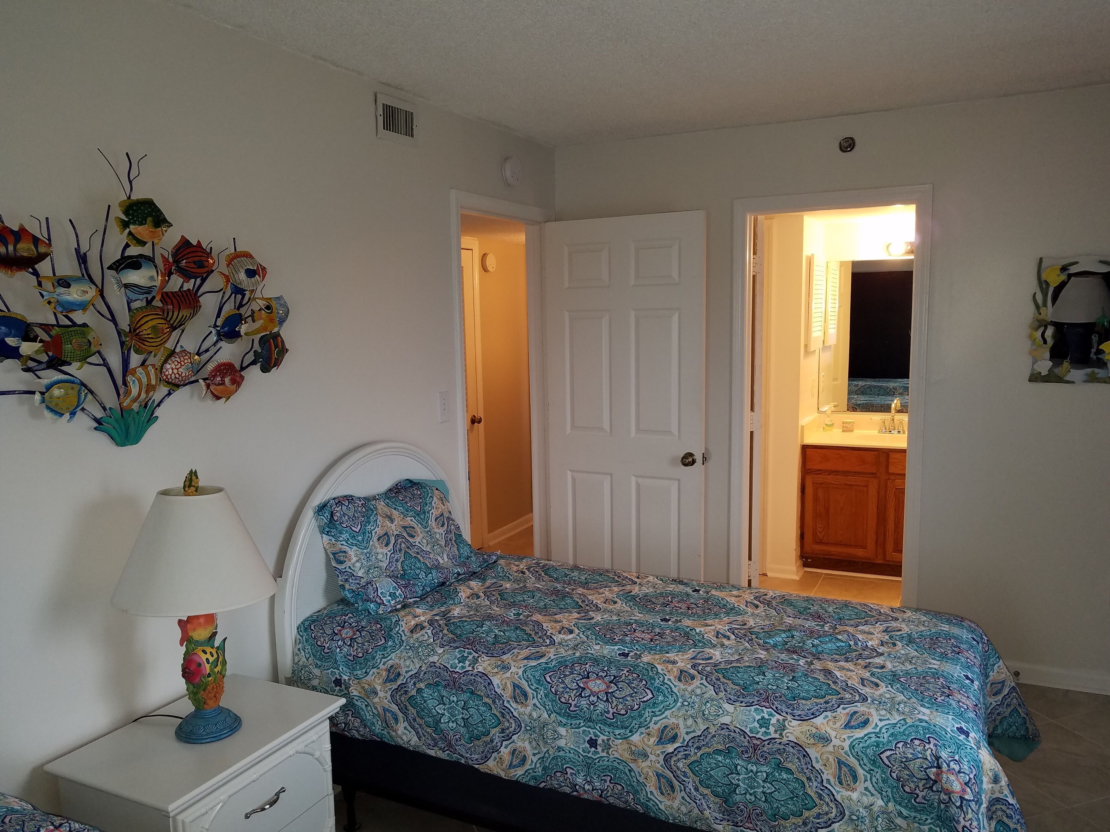 A bedroom with a bed, a nightstand, a lamp, and a wall decoration.