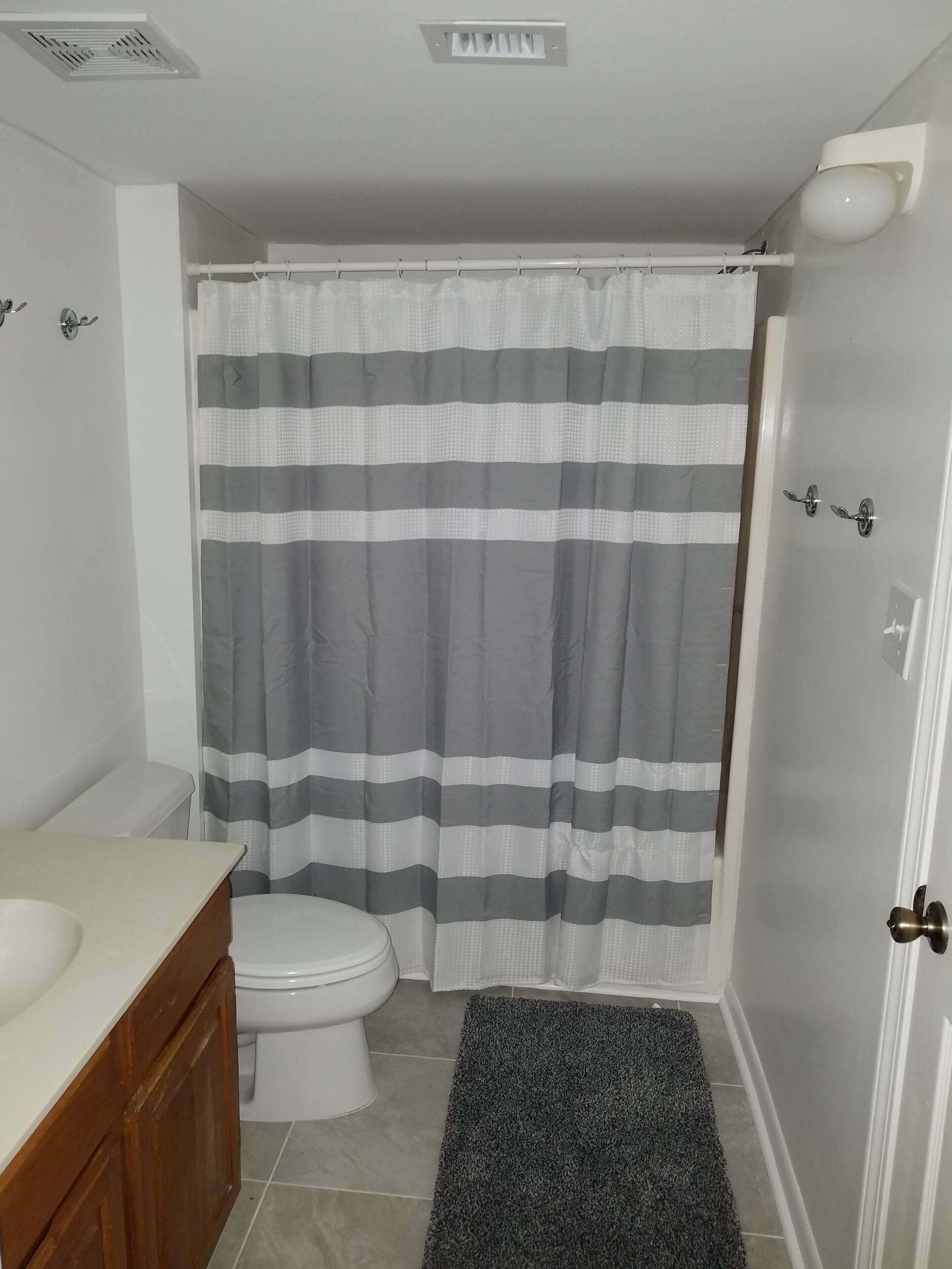 A bathroom with a toilet, a sink, a wooden cabinet, a striped shower curtain, and a dark rug.