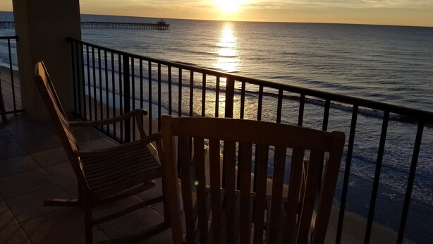 Eine Holzbank und Geländer mit Blick auf einen Sonnenuntergang über dem Meer.