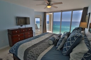 Un dormitorio con cama, televisor, cómoda y balcón con vista al océano.