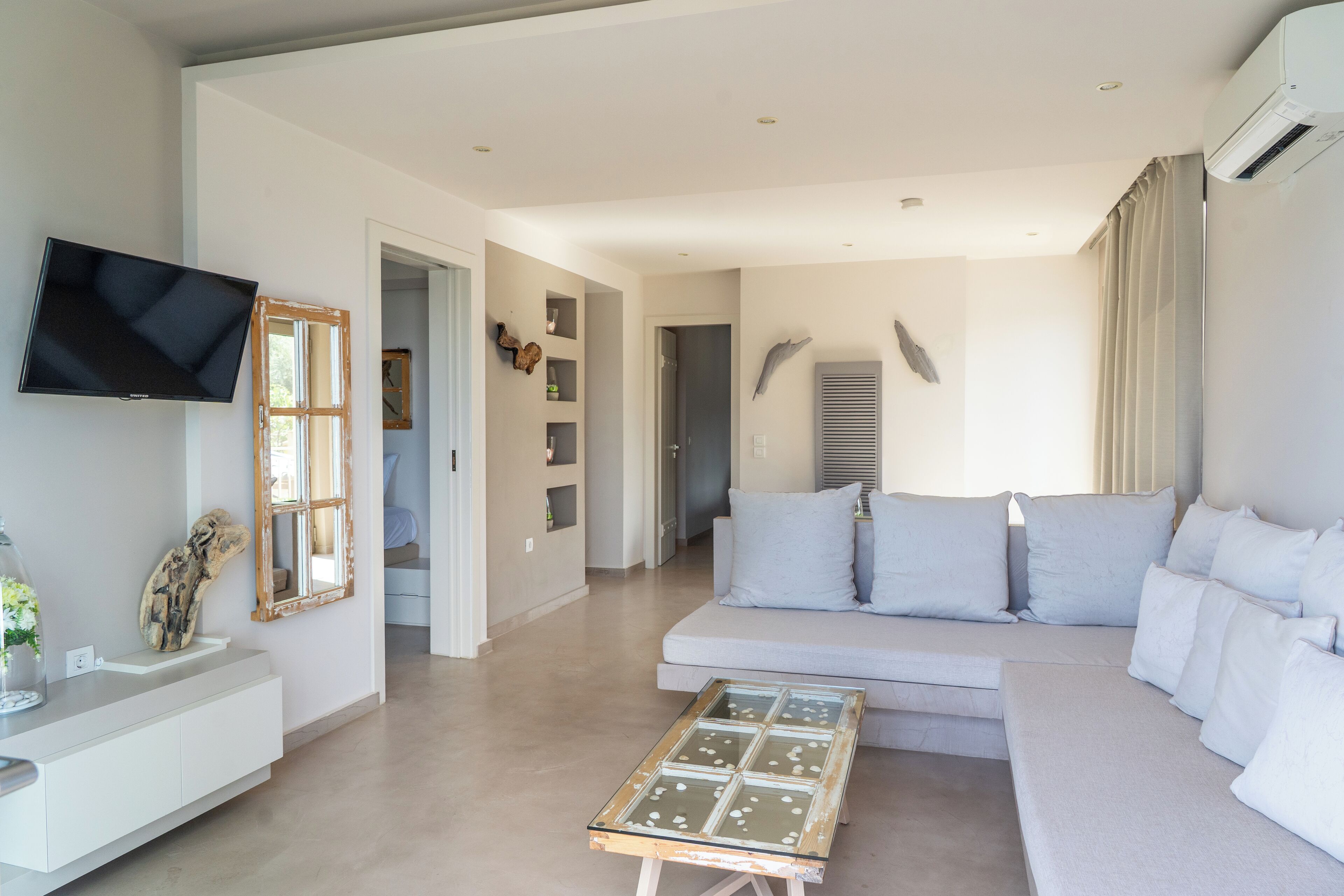 Ein stilvolles Wohnzimmer mit einem weißen Sofa, einem Glastisch und einem an der Wand befestigten Flachbildfernseher.
