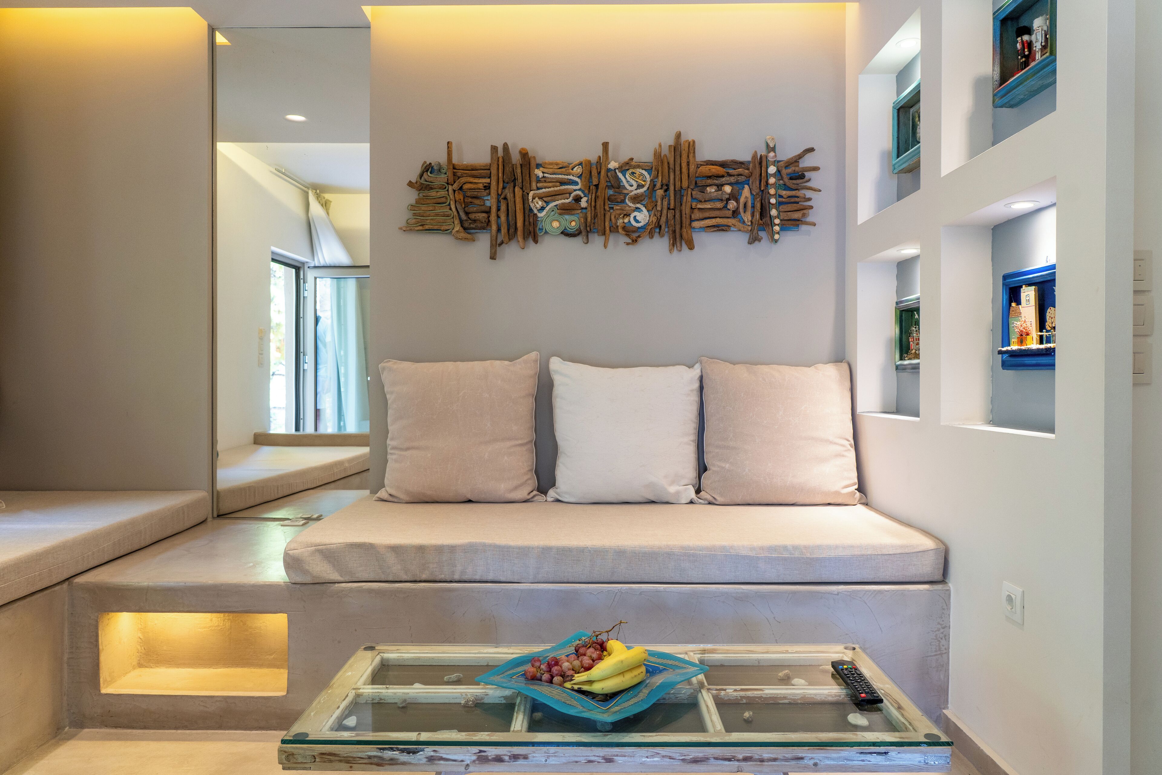 A modern living room with a sofa, a glass coffee table with fruit, and a wall art piece.