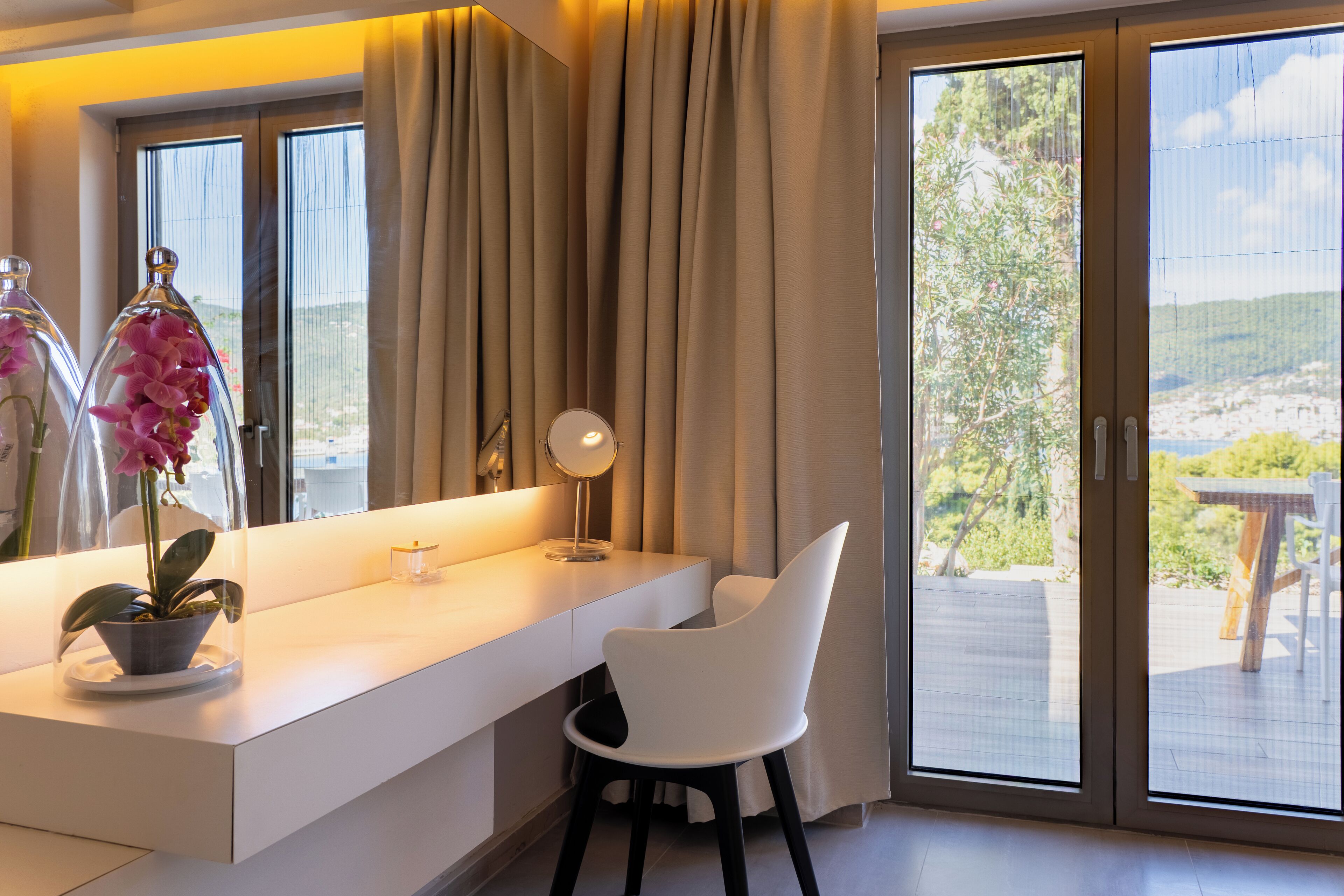 Un baño moderno con tocador blanco, un espejo y una orquídea en maceta.