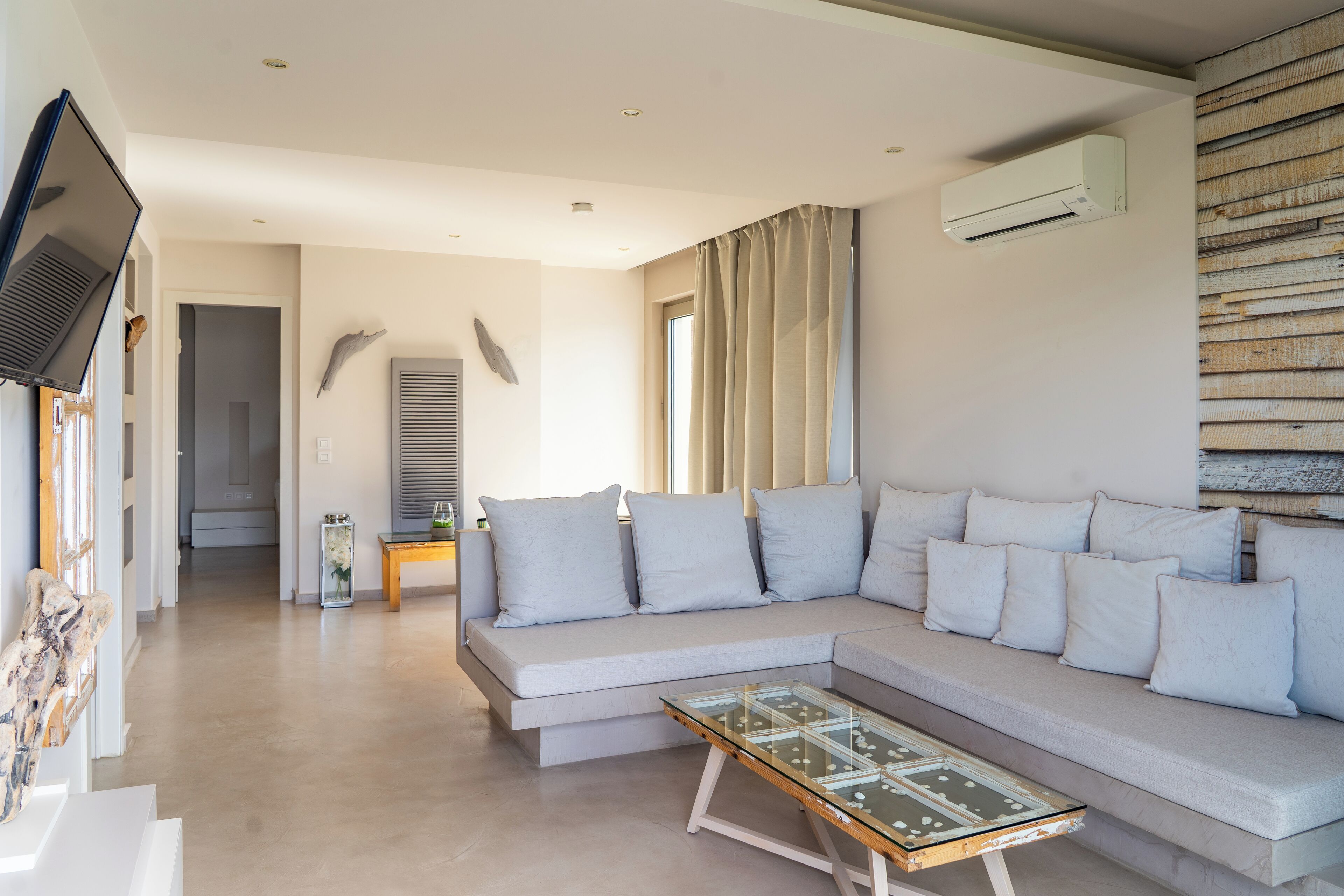 A modern living room with a large L-shaped sofa, a glass coffee table, and a flat-screen TV mounted on the wall.