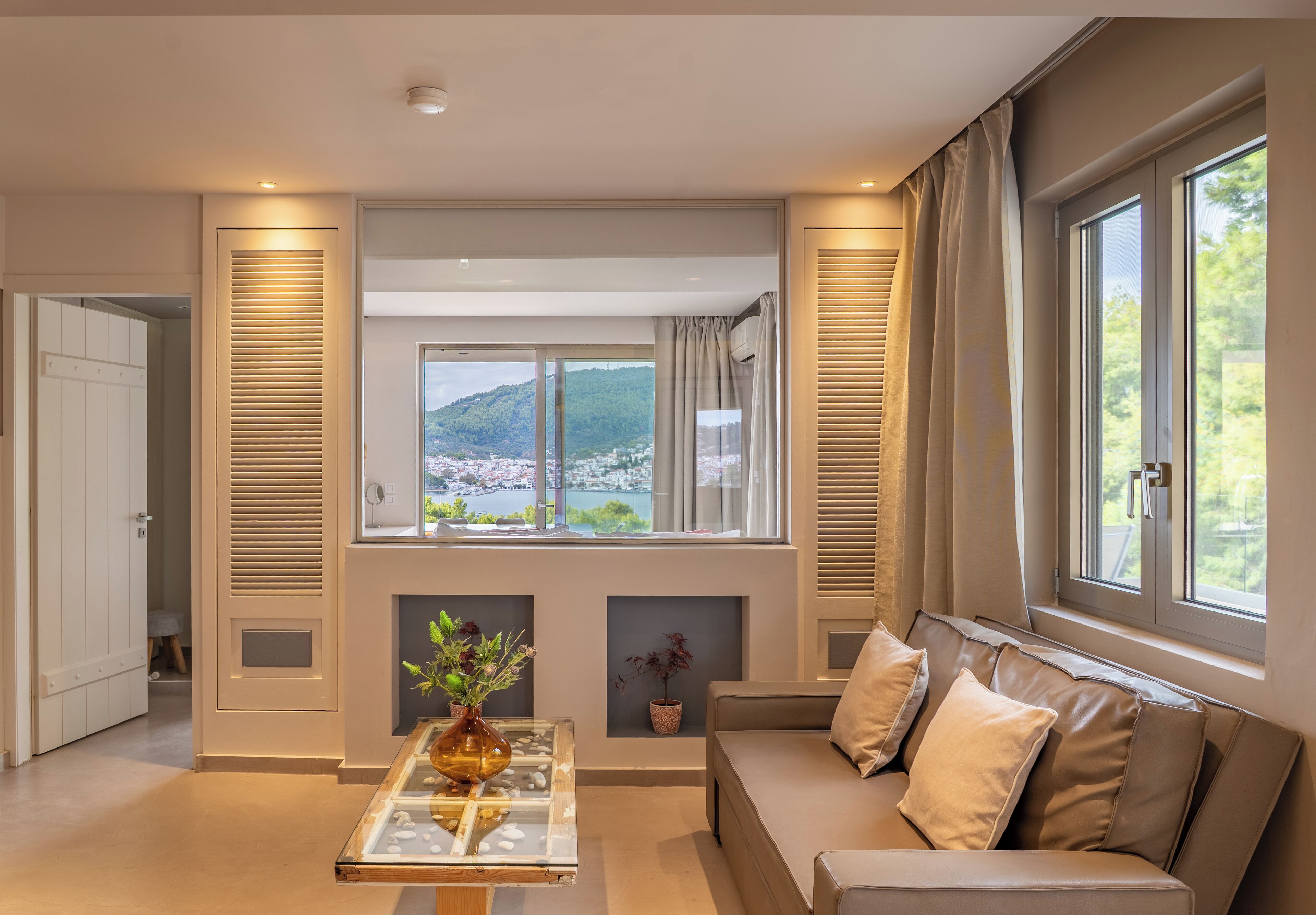 Uma sala de estar moderna com um sofá, uma mesa de centro de vidro e vista para uma paisagem montanhosa através de grandes janelas.