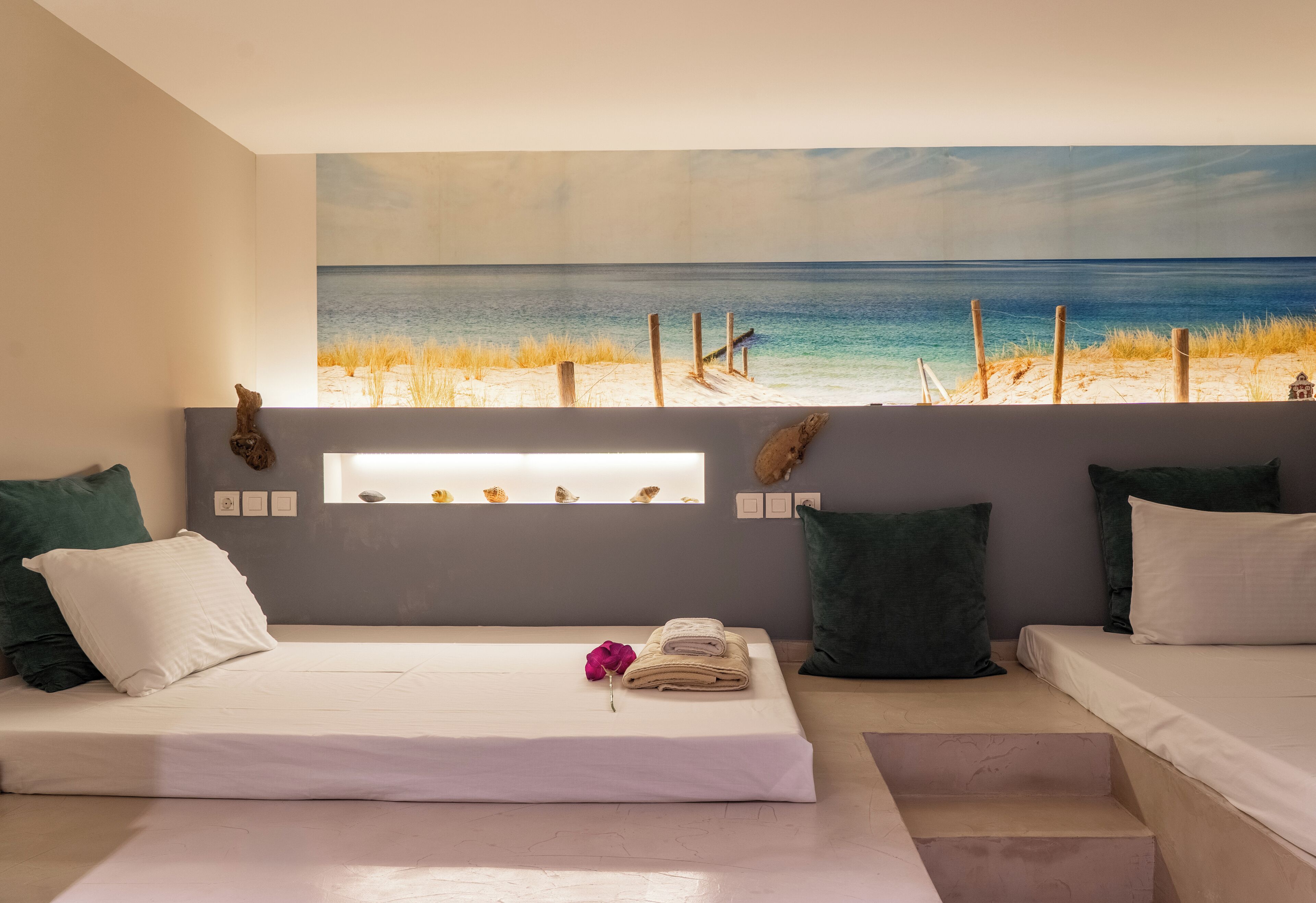 A bedroom with a large beach view painting, a bed with white linens, and two green pillows.