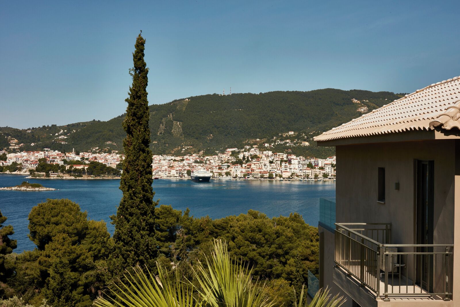 Un pueblo costero con vista despejada al mar, un árbol alto y destacado, y un edificio con balcón.