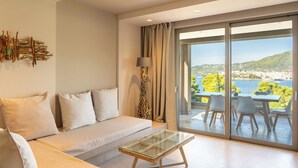 A modern living room with a sofa, a glass coffee table, and a view of a balcony with outdoor seating. - Core Luxury Suites (Skiathos)