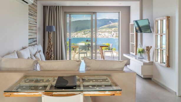 A modern living room with a sofa, a glass coffee table, and a view of a coastal landscape. - Core Luxury Suites (Skiathos)