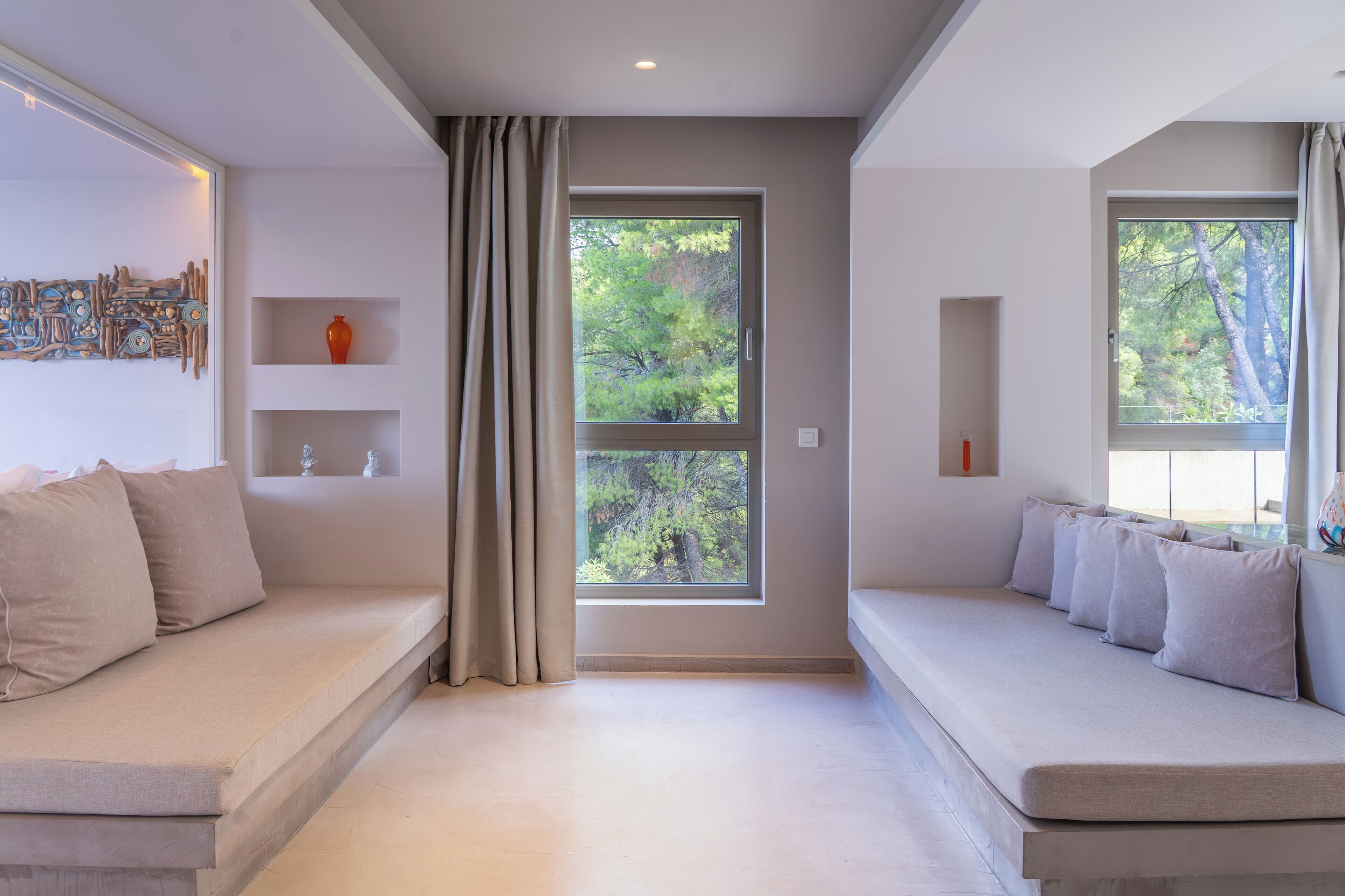 A modern living room with a beige sofa, a large window with a view of trees, and a decorative wall piece.