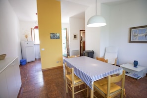 A dining area with a table set for four, a chair, a small table with a lamp, and a wall-mounted picture.
