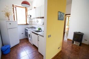 A kitchen with white cabinets, a stove, a sink, and a washing machine. There is a window with a view of greenery outside.