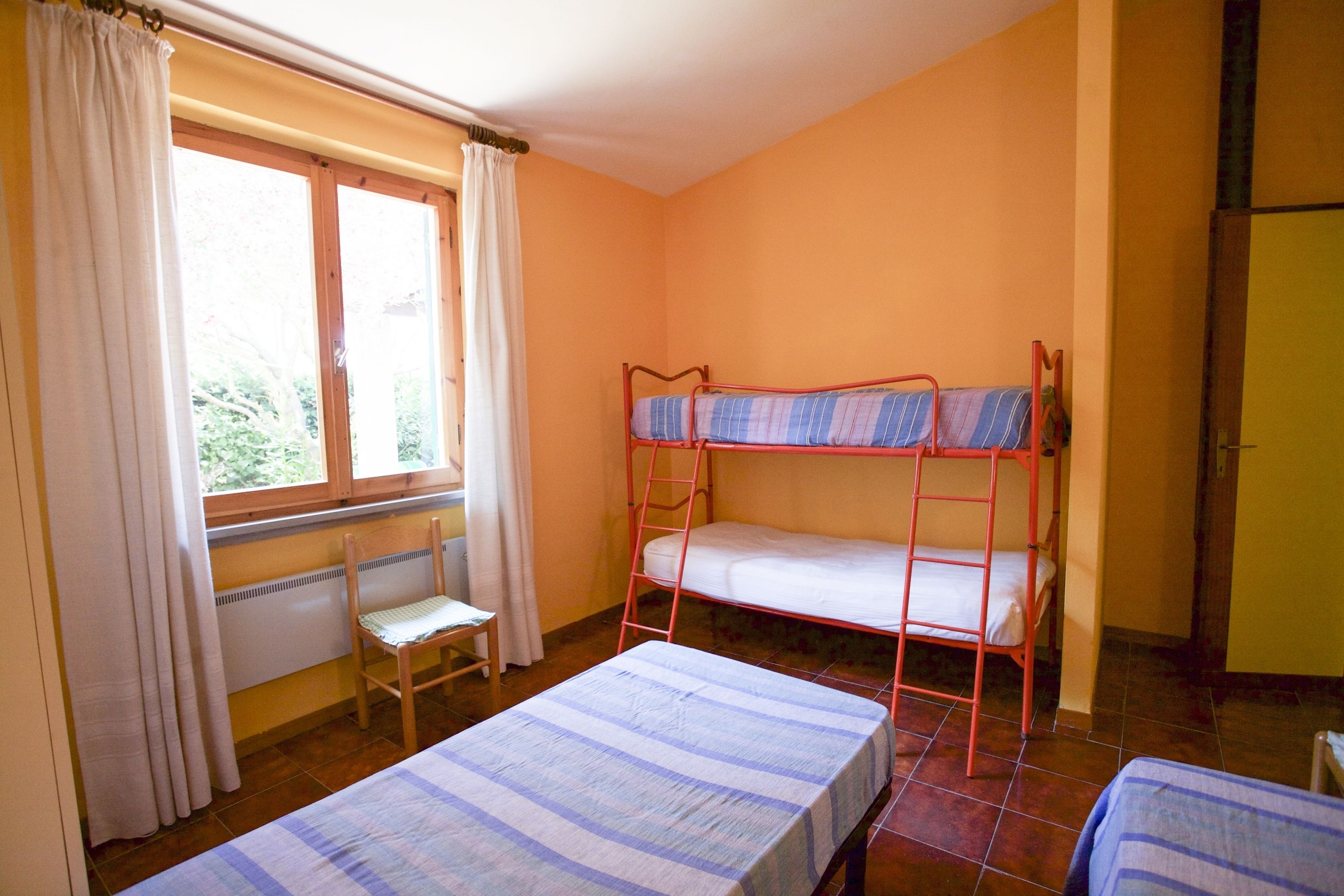 A room with a bunk bed, a single bed, a chair, and a window with curtains.