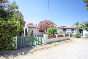 A residential property with a gated entrance, a white building with a tiled roof, and a tree with pink flowers.