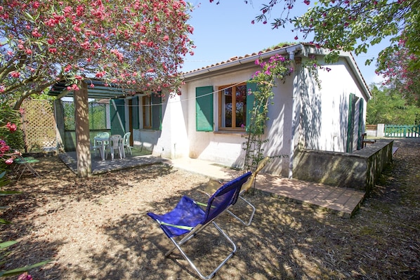 A small house with a patio, a blue chair, and a garden with pink flowers.