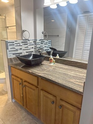 Une salle de bain moderne avec un grand miroir, un lavabo noir sur colonne et des meubles en bois.