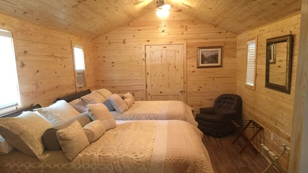 A wooden cabin bedroom with two beds, a chair, and a door. - Cabin #3, NASHVILLE, Memphis, Kentucky Lake, Birdsong , Loretta Lynns, Paris Tn (Camden)