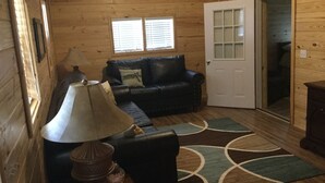 A cozy cabin interior with a wooden ceiling, a black leather sofa, a lamp, and a patterned rug. - Cabin #3, NASHVILLE, Memphis, Kentucky Lake, Birdsong , Loretta Lynns, Paris Tn (Camden)