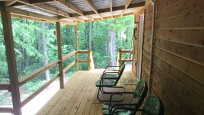 A covered outdoor seating area with wooden flooring and metal chairs, overlooking a forested area. - Cabin #3, NASHVILLE, Memphis, Kentucky Lake, Birdsong , Loretta Lynns, Paris Tn (Camden)