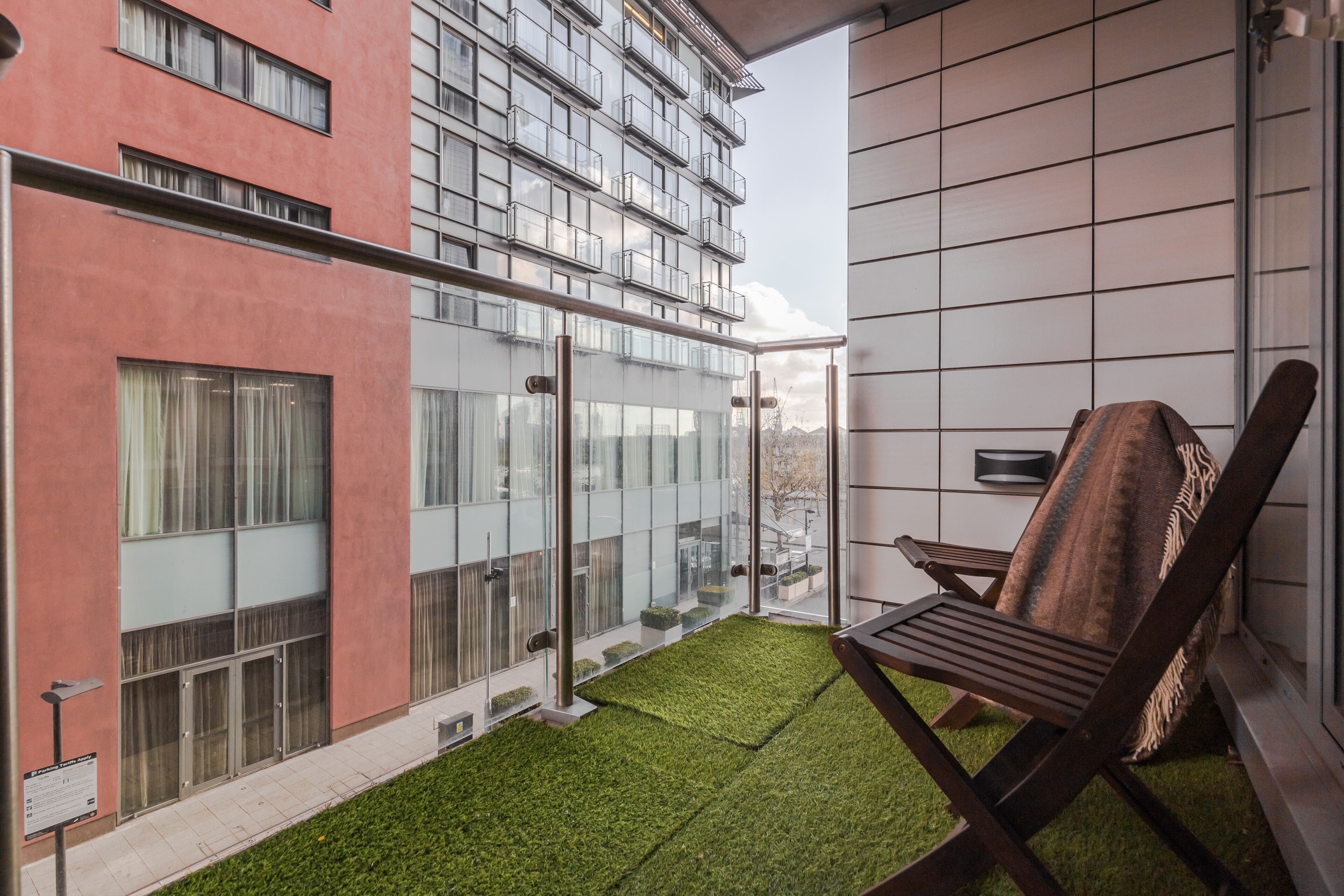 Un balcon donnant sur un immeuble moderne, une porte vitrée et une chaise en bois.