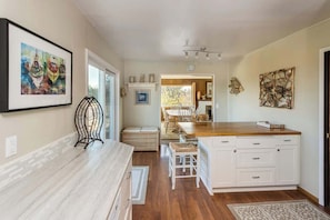 A kitchen with a wooden countertop, white cabinetry, a dining area with chairs, and a view through a glass door.