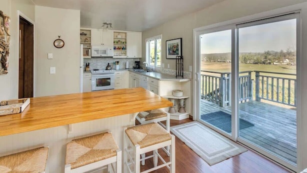 Une cuisine avec un bar en bois, des armoires blanches et une vue sur une terrasse accessible par des portes vitrées.
