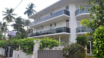 Un hotel de varios pisos con balcones, un letrero que indica habitaciones y desayuno, y abundante vegetación alrededor.