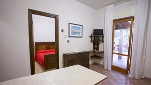 A room with a bed, a table, a TV, and a door leading to an outdoor area. - Appartamenti Bagnaia (Portoferraio)
