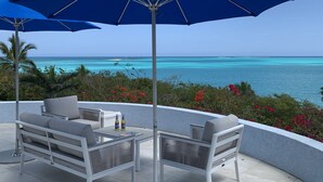 A patio with two white wicker chairs and a table, two blue umbrellas, and a view of the ocean. - Paradise! Private Beachfront Home w/ Pool & Beach WiFi!  

 (George Town)