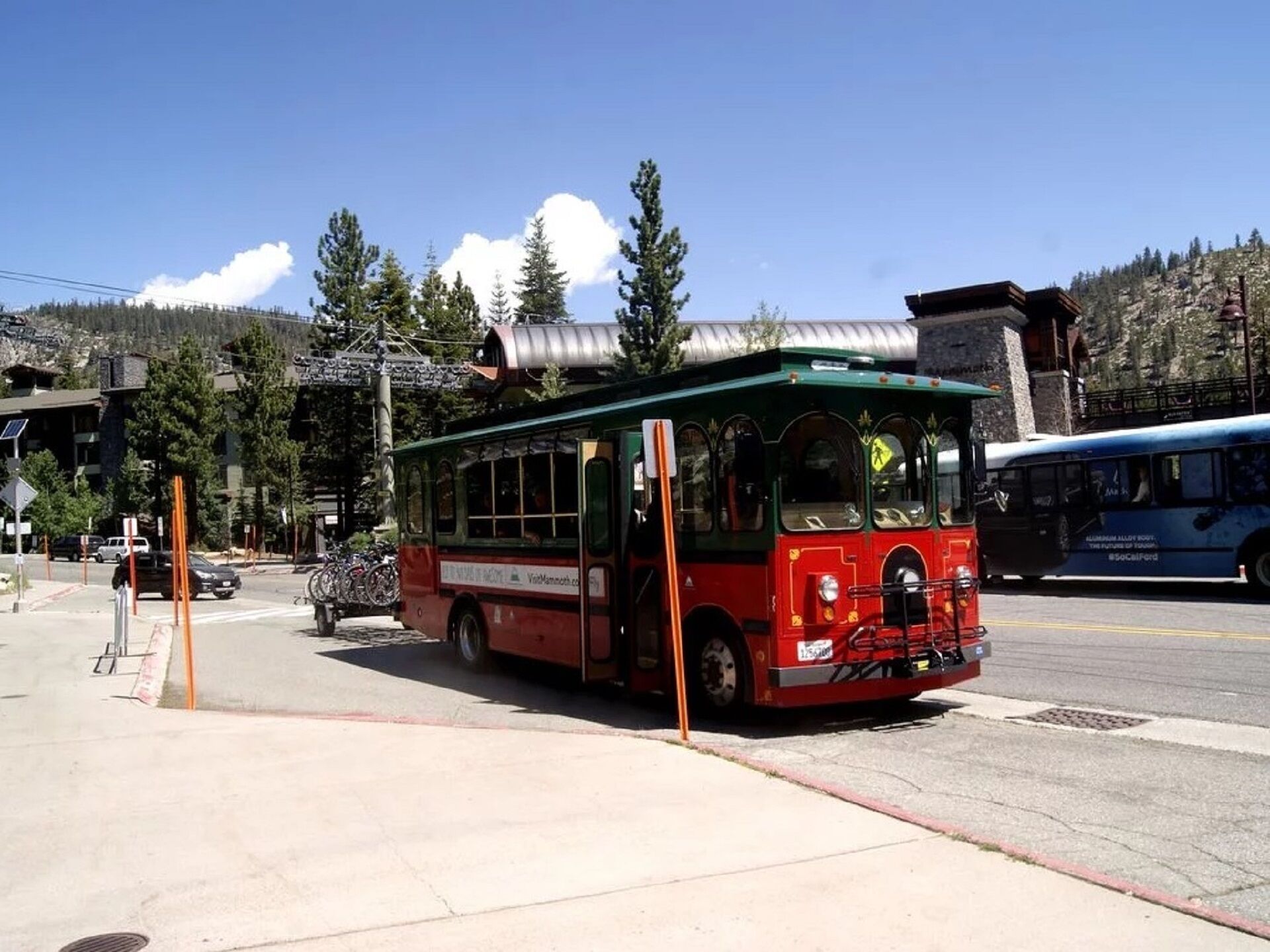 Eine rote und grüne Straßenbahn an einer Haltestelle mit blauem Himmel und Bergen im Hintergrund.