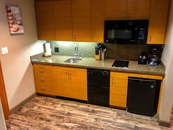 A compact kitchen with wooden cabinets, a stainless steel sink, a microwave, and a dishwasher.