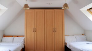 Quarto com um grande guarda-roupa de madeira, duas camas com roupa de cama branca e luminárias pendentes.