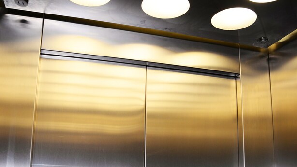 Interior de elevador com paredes metálicas e iluminaç ão no teto.
