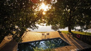 A wooden deck with a pool, surrounded by trees and a view of the water. - Chundu Island (Victoria Falls)