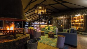 A cozy lounge area with a stone fire pit, comfortable seating, and a wine rack. - Chundu Island (Victoria Falls)