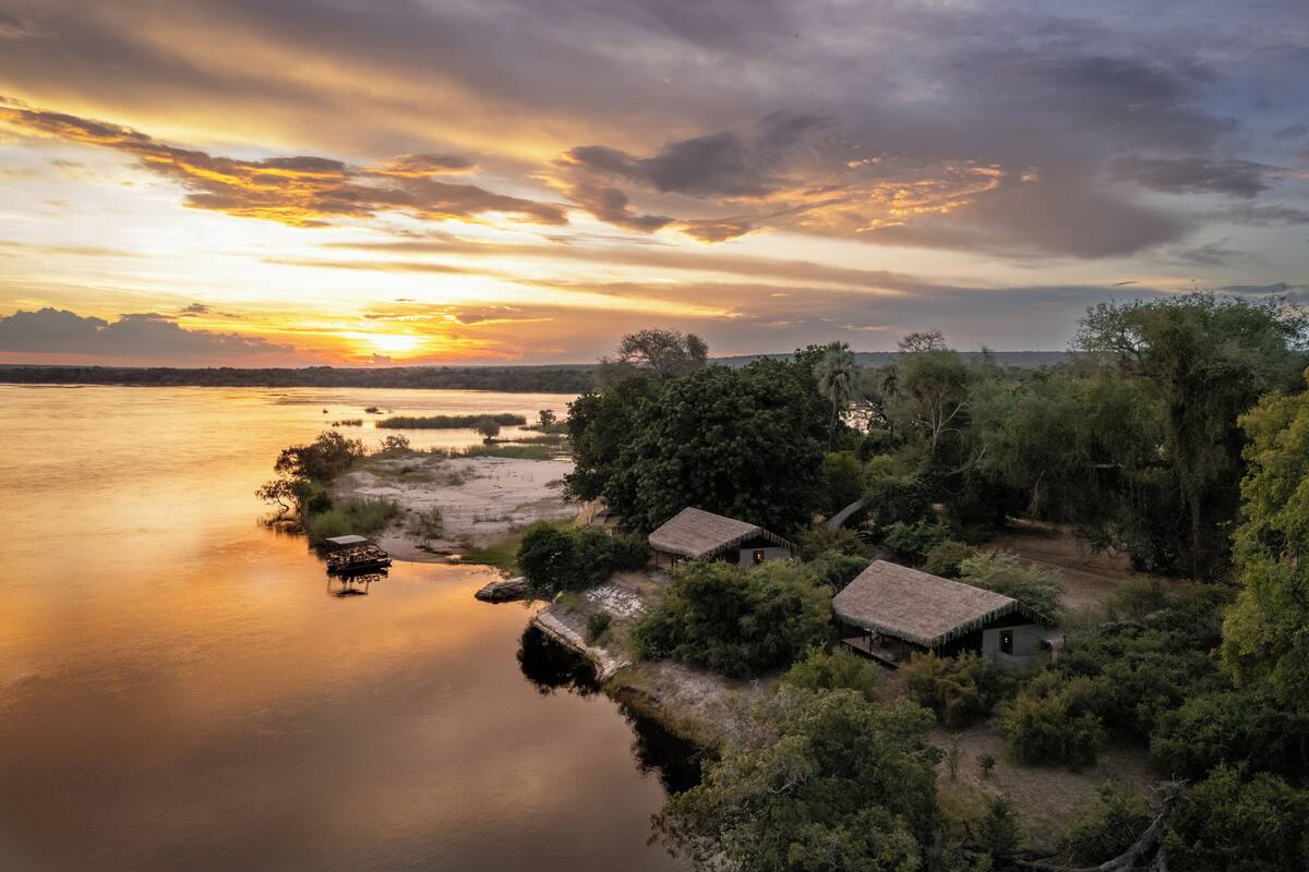 A tranquil riverside village with traditional huts, calm water, and a sunset.