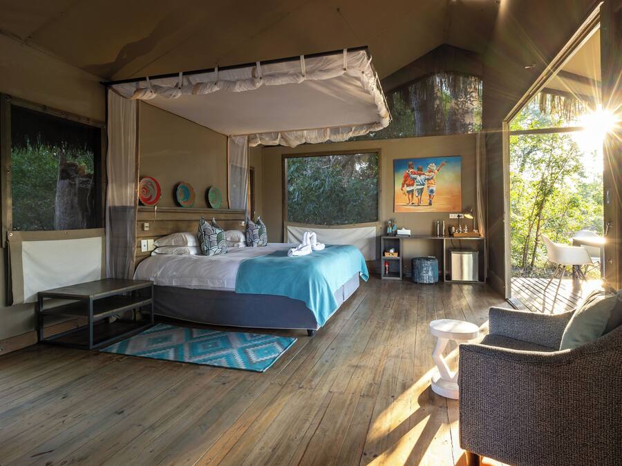A bedroom with a canopy bed, a sitting area with a chair and table, and a painting on the wall.