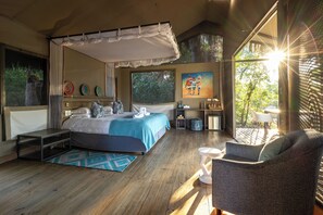 A bedroom with a canopy bed, a sitting area with a chair and table, and a painting on the wall. - Chundu Island (Victoria Falls)