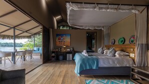 A bedroom with a large bed, a desk, and a view of a lake. - Chundu Island (Victoria Falls)
