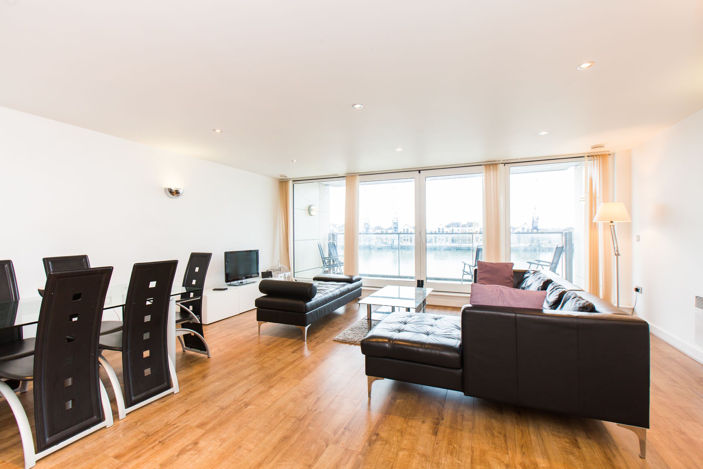 A modern living room with a sofa, chairs, a TV, and large windows offering a city view.