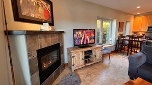 A living room with a fireplace, a television, a dining area, and a kitchen. - CLEAN-MODERN-WIFI-HARBOUR & MTN VIEWS-SPACIOUS-SHORT WALK TO TOWN & BEACH TRAILS (ucluelet)