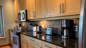 A modern kitchen with wooden cabinets, stainless steel appliances, and a black countertop. - CLEAN-MODERN-WIFI-HARBOUR & MTN VIEWS-SPACIOUS-SHORT WALK TO TOWN & BEACH TRAILS (ucluelet)
