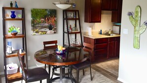 A dining area with a round glass table, wooden chairs, and a chandelier. There are shelves with decorative items and a painting of a garden scene. - Old Town Desert Retreat (Scottsdale)