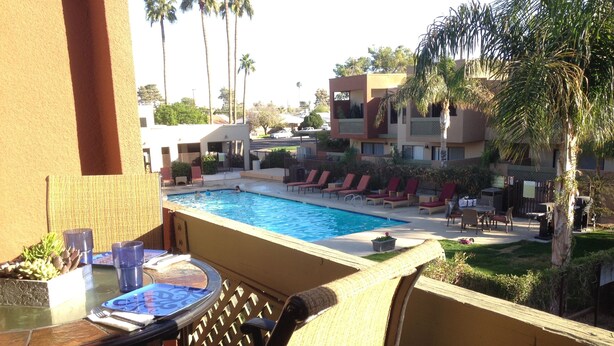 A poolside area with a table and chairs, a pool, and a view of the surrounding buildings and palm trees. - Old Town Desert Retreat (Scottsdale)
